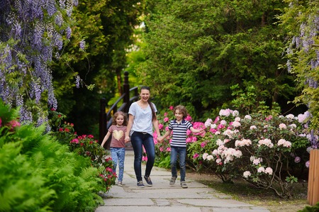 Mom walks in the lush park with her daughter and son. Detyat 7-8 years. Beautiful weather and beautiful nature. All cheerfully laugh. The best way to vacation for children's healthの写真素材