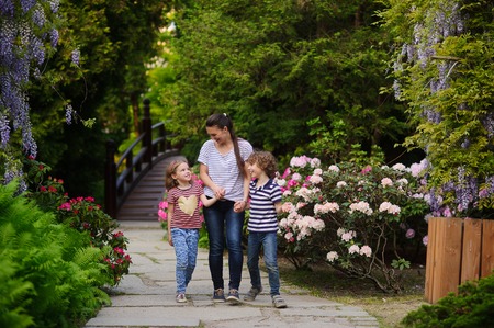 A woman walks in the park with their son and daughter. She holds them by the hand and tells something. Family looks happy in the beautiful surroundings. Free time in nature is useful for allの写真素材