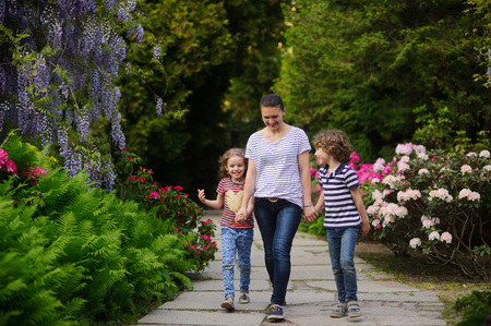 Young mother led to the park daughter and a son. Children 7-8 years of age. Family walking on path blooming garden. They are fun to talk to. Mom tries to spend more time with their children outdoors. She cares about the health of the familyの写真素材
