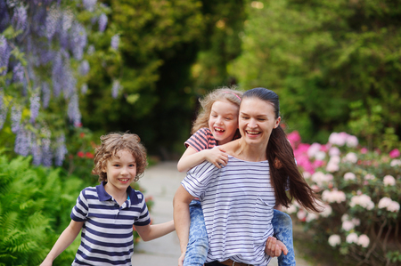 Family walking garden paths. Girl tired of walking, the boy running with joy. Walking in the fresh air are good for health. Mother happy. It teaches children to love natureの写真素材
