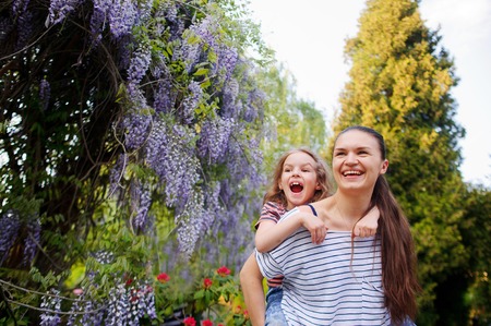 Mother and daughter walking in the summer park. A woman carries a girl on his shoulders. They admire nature. The mother takes care of the spiritual and physical health of the childの写真素材