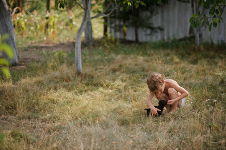 The little boy irons a tiny puppy. The child squats. Before him a tiny black puppy. The boy tenderly irons the fluffy friend.の写真素材