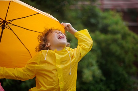 The little boy tongue catches rain drops. He has thrown back the head and has closed eyes. A hand holds an umbrella.の写真素材