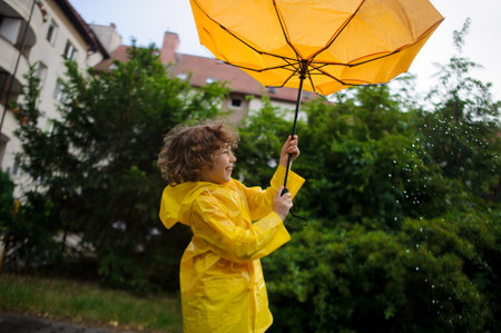 Onset of wind has wrest an umbrella in boy's hands. But it is pleasant to the child. He to stand under warm rain and laughs.の写真素材