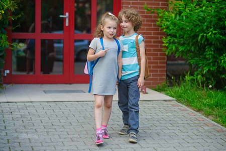 Boy and go to school having joined hands. Warm September day. Good mood. School students about something talk. On faces lovely smiles.の写真素材