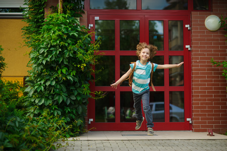 The carefree first grader rejoices to the beginning of summer vacation. He runs out from doors of school. As if flies. On a face of the school student expression of happiness.の写真素材