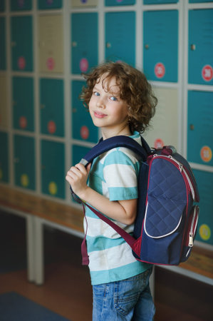 Elementary school student standing near lockers in school hallway. Behind kid's school backpack. The...