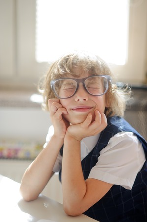 Funny little schoolboy in huge glasses has fallen into a reverie. The child propped head in his hands and closed his eyes. It is a disciple of an elementary school. Back to school.の写真素材
