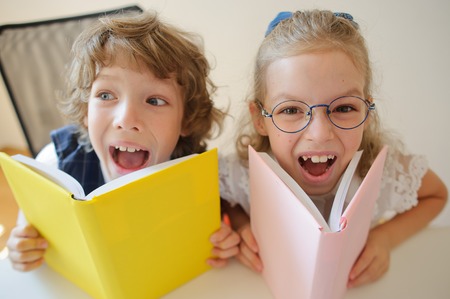 Two young classmate, boy and girl, are sitting at the same desk. Children learn in elementary school. In the hands of the students open textbooks. Kids fun look into the camera. Back to school.の写真素材