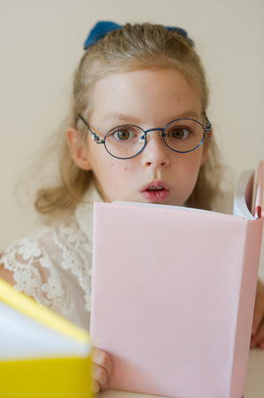 Lovely small student reads. Schoolgirl bespectacled holds the textbook. She has serious look.の写真素材
