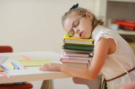 Little schoolgirl fall asleep on a pile of books. Tired girl with glasses rested her head on the book. To kids difficultly long to be engaged.の写真素材