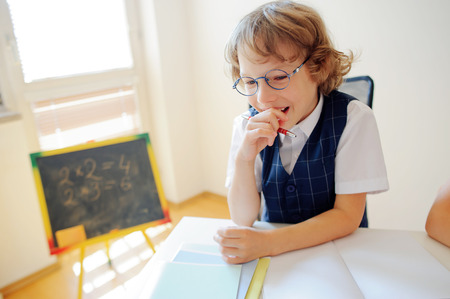 Cute little schoolboy in glasses has fallen into a reverie. The boy leaned his head on his hand and looking somewhere to the side. This elementary school student. Back to school.の写真素材