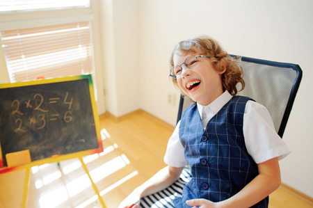 Funny little schoolboy in glasses cheerfully laughs. This elementary school student. Nearby is a small blackboard. Back to school.の写真素材
