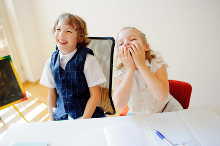Funny little schoolchildren, boy and girl, sit at one desk. It's elementary school students. Children laugh. On the desk in children are school supplies and textbooks. Back to school.の写真素材