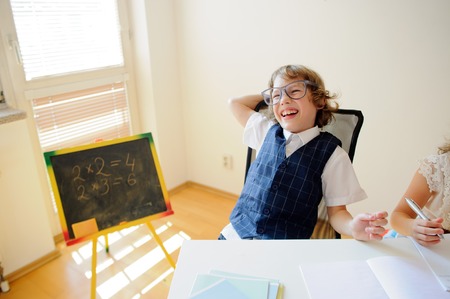 Naughty little schoolboy in glasses cheerfully laughs. This elementary school student. Near to a school desk of the child there is a small blackboard. Back to school.の写真素材