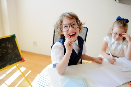 Funny little schoolchildren in glasses, boy and girl, sit at one desk. It's elementary school students. Children laugh. The deskmate in children are school supplies and textbooks. Back to school.の写真素材