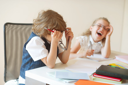 Disciples of an elementary school, boy and girl, are sitting at the same desk. Children are very fun, they laugh. On the desk in children are school supplies and textbooks. Back to school.の写真素材