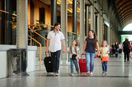 Young family with two children at train station. The family passes through the big waiting room. The daddy holds by the hand the son, mother-the daughter. All in a good mood. Parents smiling.の写真素材