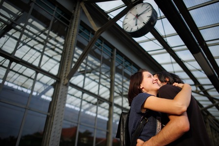 Loving couple met or parted on the platform under the clock. The young man put his arm around the girl. Girl smiling happily.の写真素材