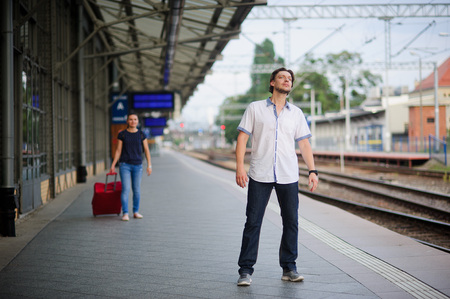 Young man on the platform waiting for someone. He anxiously peering into the distance. Behind him hurrying young woman with a suitcase.の写真素材