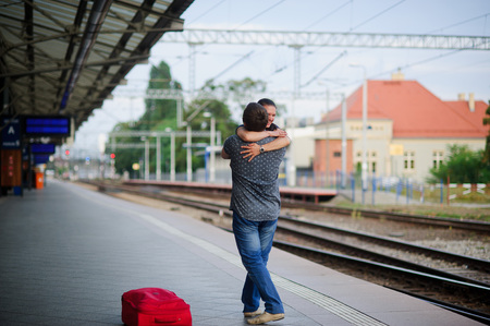 Joyful meeting at the railway station. The young man easily lifted the girl. She hugged him tightly. On a girl's face happy smile. Nearby the red suitcase has fallen.の写真素材