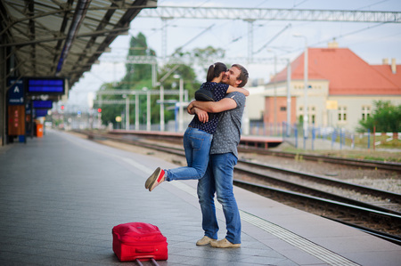 On the empty platform joyful meeting. Young man easily picked up on the hands of the girl. On his face a happy smile. Nearby is the red suitcase.の写真素材