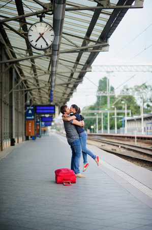 Joyful meeting at the railway station. The young man lifted the girl. Couple hugging and kissing. Nearby the red suitcase has fallen.の写真素材