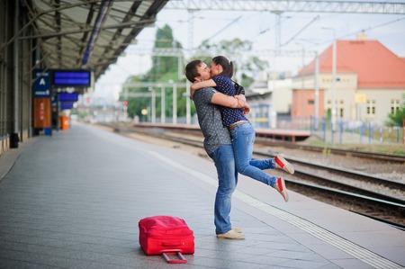 Joyful meeting at the railway station. The young man lifted the girl. Couple hugging and kissing. Nearby the red suitcase has fallen.の写真素材