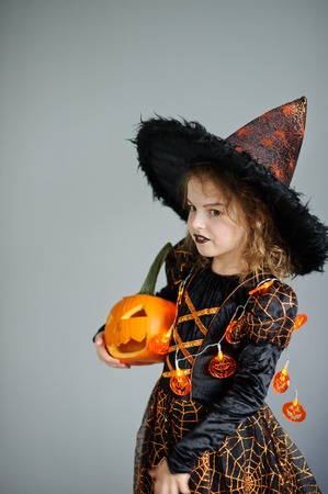 Halloween. Girl portray evil sorceress.She is wearing black-and-orange dress and hat. From under his hat sticking disheveled hair. Girl has an evil expression. In hands at her pumpkin - Jack o lanternの写真素材