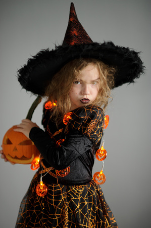 Halloween. Girl portray evil sorceress. She is wearing a black-and-orange dress and hat. From under his hat sticking disheveled hair. Girl has an evil expression. In hands at her pumpkin - Jack o lanternの写真素材
