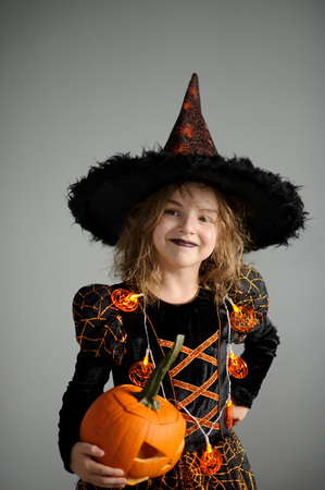 Halloween. Girl portray evil sorceress. She is wearing black-and-orange dress and hat.From under his hat sticking disheveled hair. Girl has an evil expression. In hands at her pumpkin - Jack o lanternの写真素材