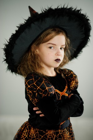 Preparation for Halloween. Beautiful girl 8-9 years shows the evil witch. She is dressed in black and orange dress and a big hat. On the face of the appropriate makeup. Children adore Halloween.の写真素材