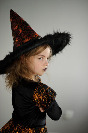 Preparation for Halloween. Cute girl 8-9 years shows the evil fairy. She is dressed in black and...