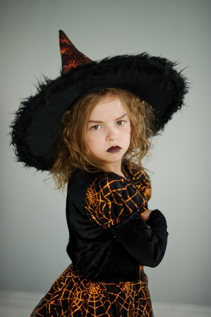 Preparation for Halloween. Cute girl 8-9 years in image the evil fairy. She is dressed in black and orange dress and a big hat. From under a hat a wild hair sticks out. Children adore Halloweenの写真素材