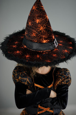 Halloween Party. Girl in image the evil sorcerer. She is dressed in black-orange dress. Wide-brimmed...