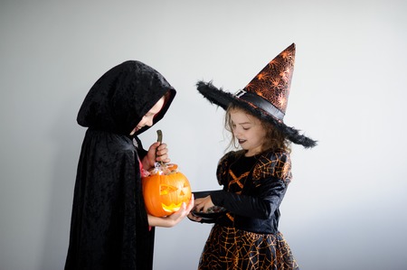 Trick or Treat. Boy and girl in suits for Halloween. They in image powers of darkness. Girl - evil fairy, boy - warlock. Girl holds sweets in hands. Boy holds pumpkin - Jack o lantern. Booの写真素材