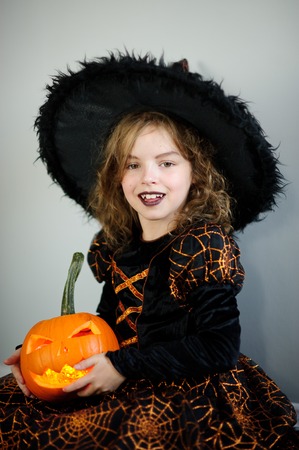 Beautiful girl of younger school age in an image of the evil witch. Girl has dressed up by Halloween. In hands at her orange pumpkin - Jack o lantern. Children like Halloween.の写真素材