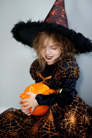 Beautiful girl of younger school age in an image of the evil witch. Girl has dressed up by Halloween. In hands at her orange pumpkin - Jack o lantern. Children like Halloween.の写真素材
