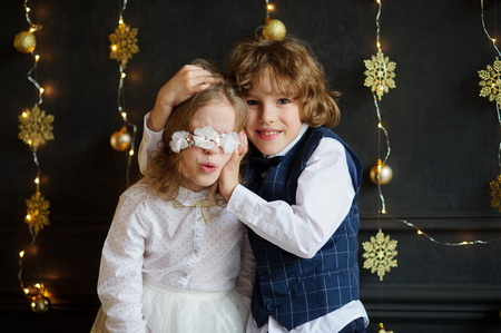 Christmas. Two festively dressed children photographed for Christmas card. Kids tired pose, they are acting up. Against the background of the dark walls, decorated with golden Christmas lights.の写真素材