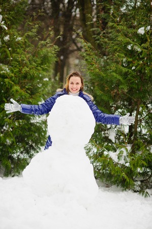 White Christmas. Cute young woman builds a big snowman in the park. To her it is very cheerful. The woman without headdress. It is snowing. All ground in the park is covered with snow.の写真素材