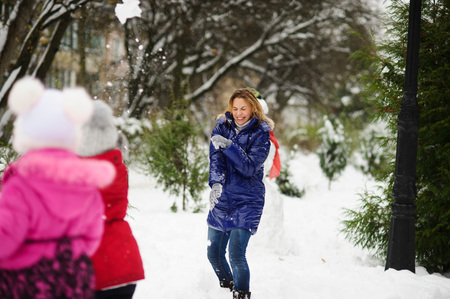 White Christmas. Girl plays with mother in snowballs in the winter park. All ground is covered with snow. On a background there is a big snowman. Mother with the daughter cheerfully spend time.の写真素材
