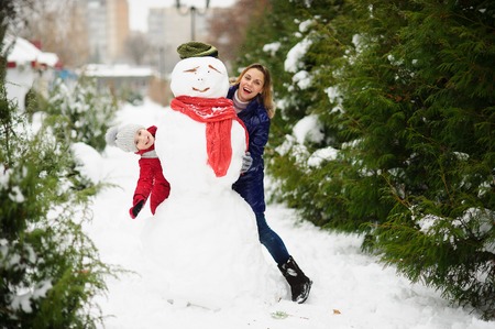 The young woman and her daughter look out because of a big snowman. In the park it is snowing. All earth is covered with fluffy snow. Mother and the daughter cheerfully spend time.の写真素材