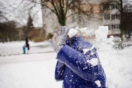 The woman turns aside from the snowballs flying to her. Someone fires at her snowballs. Her face isn't visible. She has exposed hands forward. All ground is completely covered with fluffy snow.の写真素材