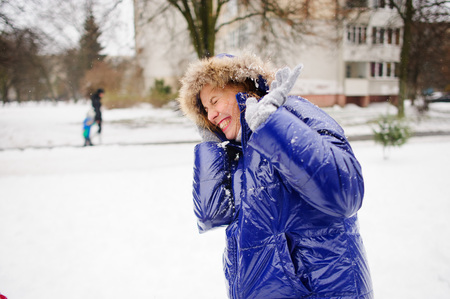 Woman turns aside from the snowballs flying to her. Someone fires at her snowballs. She pulls a hood over the face and cheerfully laughs. All ground is completely covered with fluffy snow.の写真素材
