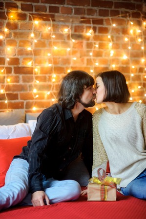 The young couple exchanges gifts. The beautiful man and the woman lie on a bed. Before them a box with a gift in beautiful packing. Young people look with love and tenderness at each other.の写真素材