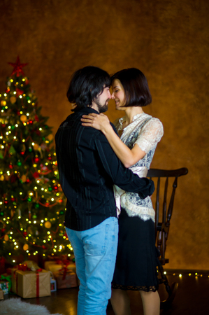 The beautiful young couple dances near the Christmas tree. Young people with love and tenderness look at each other. Under the Christmas tree there are a lot of gifts in beautiful boxes.の写真素材