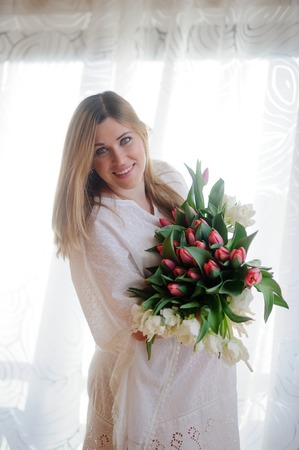 Young beautiful pregnant woman with a huge bouquet of motley tulips. She in a light white dress. On a woman's face happy smile.の写真素材