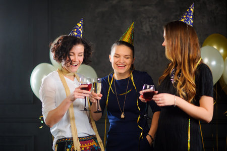 Three young women celebrate someone's birthday. In hands at everyone a glass with champagne. They...