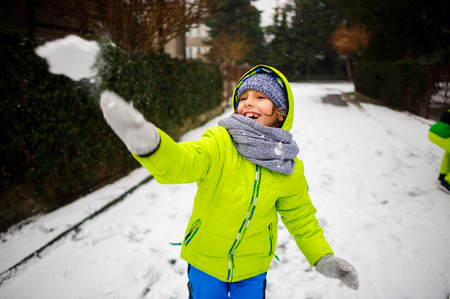 The cheerful boy of school age plays snowballs. The boy is dressed in a bright ski suit. It is snowing. To the boy it is very cheerful.の写真素材