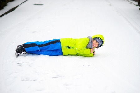 The cheerful boy of school age lies on snow. The boy is dressed in a bright ski suit. It is snowing. To the boy it is very cheerful.の写真素材